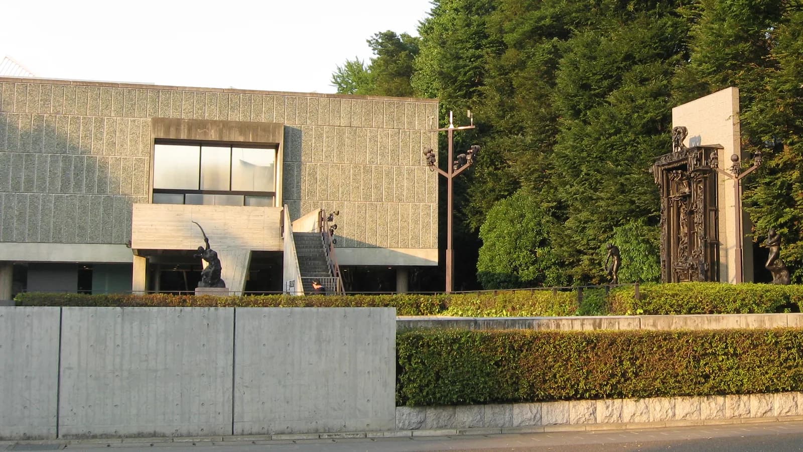 コンクリートの塀と生垣の向こうに、石を張った箱形の建物と、前庭に立つ数体のブロンズ彫刻