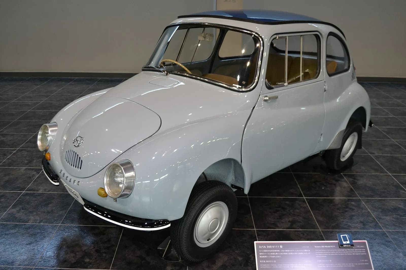 スバル360（1959年製）を斜め前から。水色の丸い小さな軽自動車。博物館の展示車