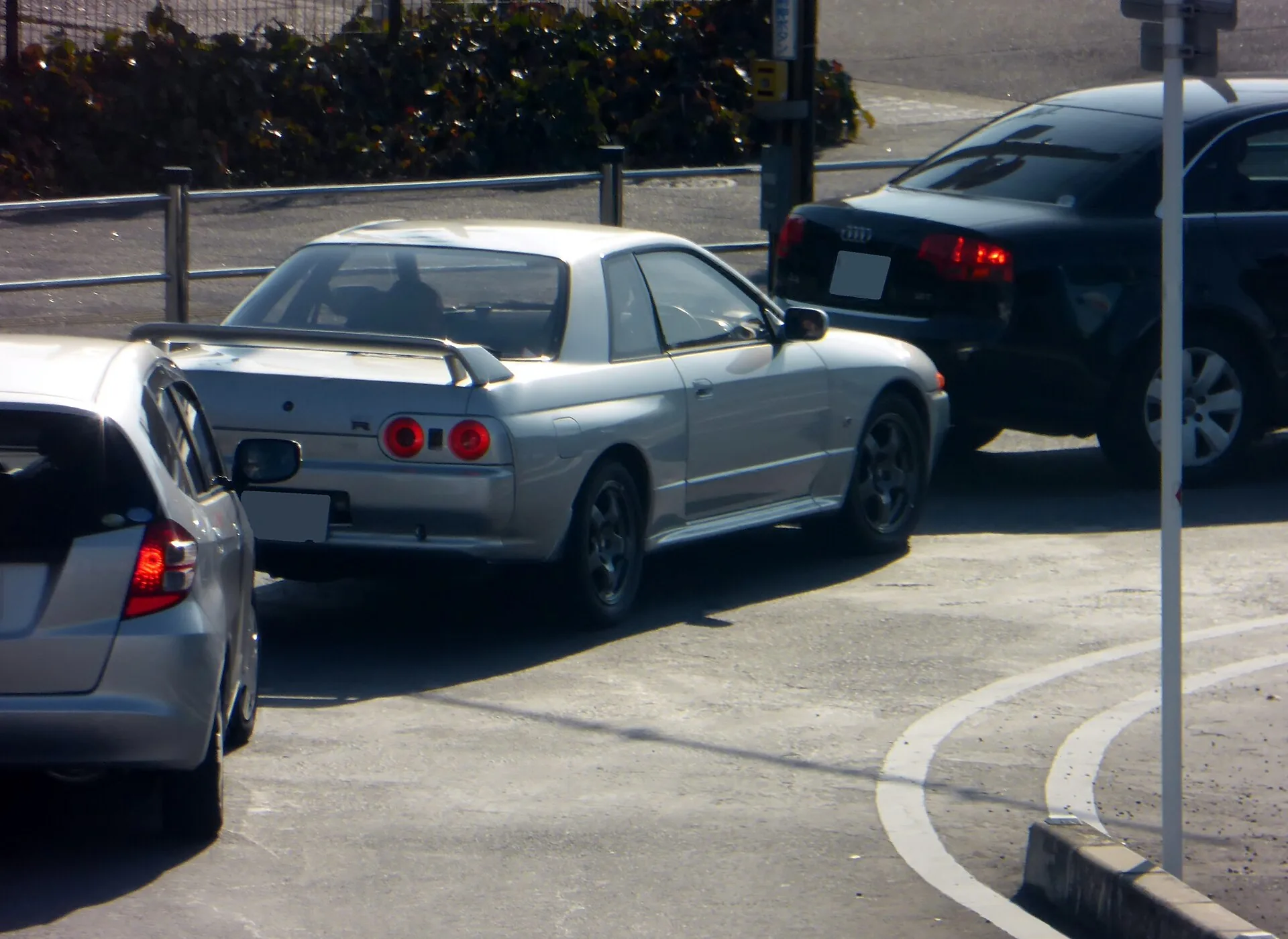 路上に停まる日産スカイラインGT-R（R32型）を後方から。銀色の車体に丸い4灯のテールランプ