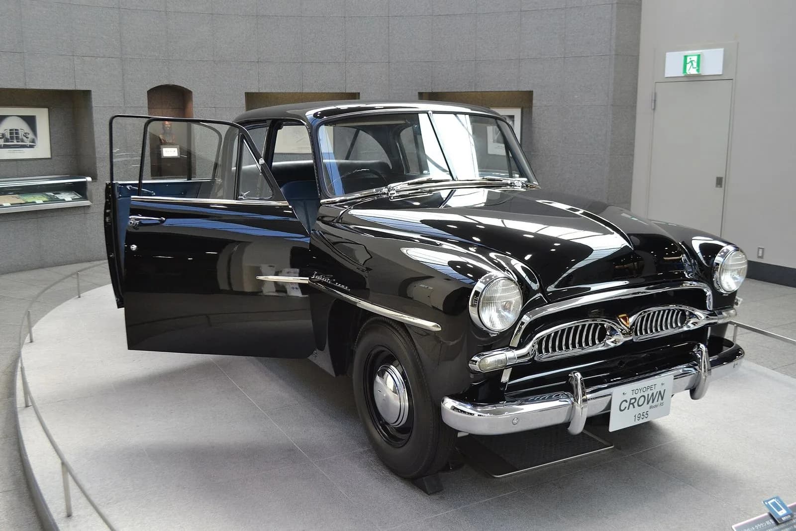 初代トヨペット・クラウン（1955年製）を斜め前から。黒いセダン。運転席側の後ろの扉が開いた展示状態