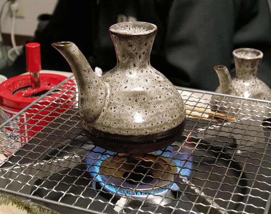 コンロの網の上で直火にかけられた陶器の燗用の酒器