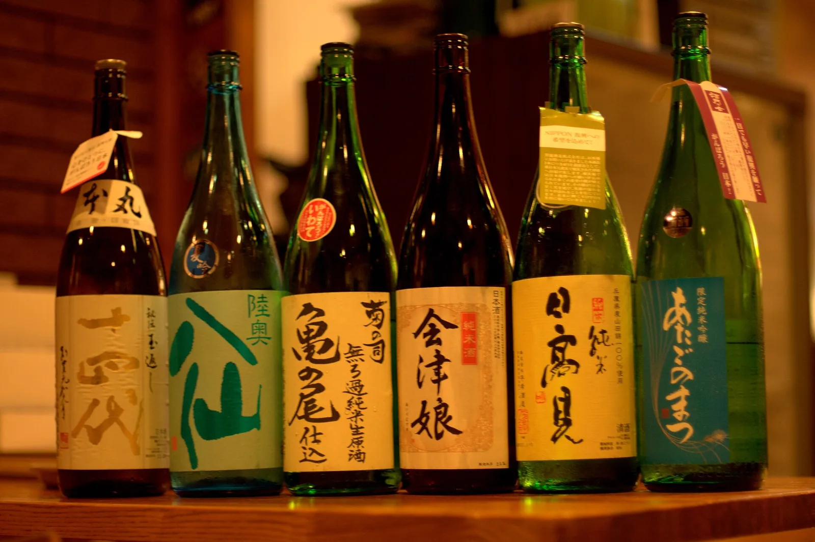飲食店の棚に並ぶ日本酒の一升瓶6本。各瓶のラベルに銘柄名