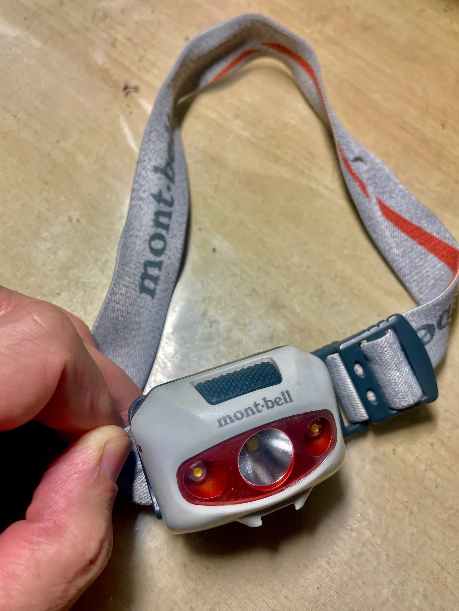 使い込まれたmont-bellのヘッドランプを手に持っている。白い本体に赤いレンズ枠、グレーのバンドにmont-bellの文字
