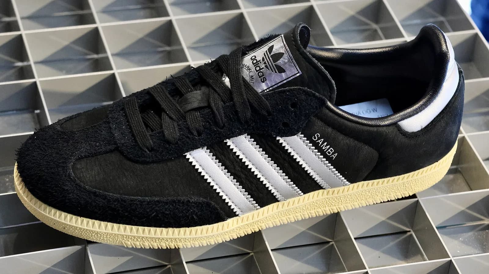 adidasの黒いサンバの真横。側面に銀の三本線とSAMBAの金文字、タンにトレフォイルのラベル