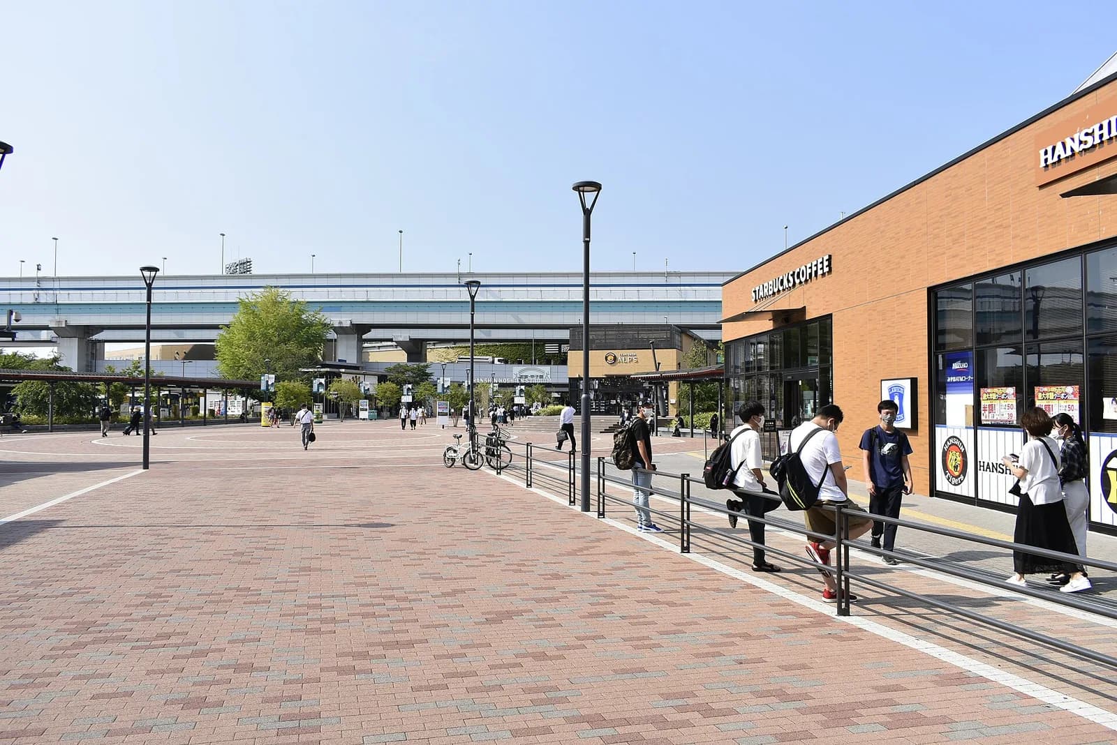 球場の外の広場。奥に阪神甲子園球場の建物と球団ショップ、右手に商業施設、上に鉄道の高架が通る