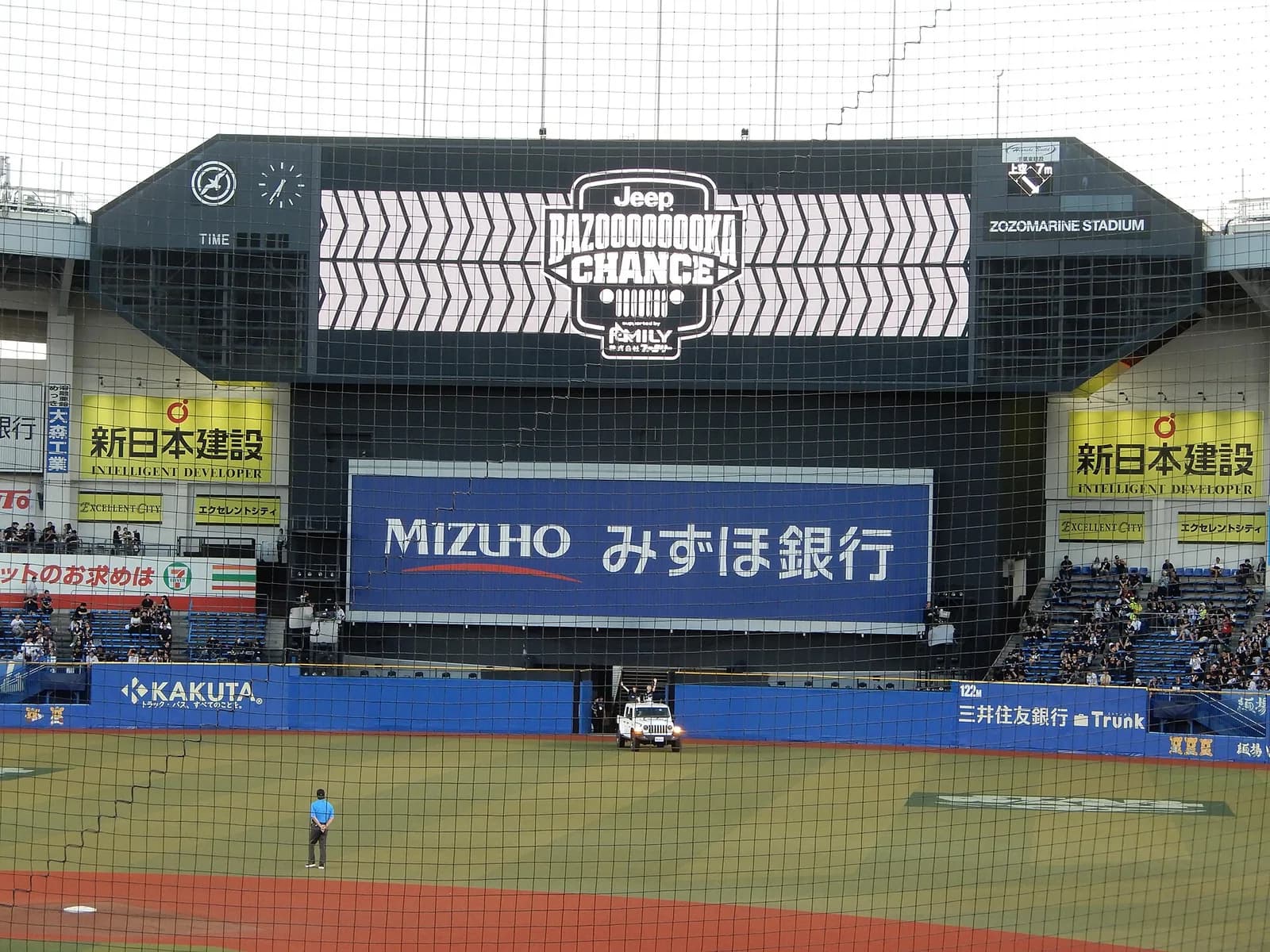 海沿いの球場の黒い大型ビジョンと外野スタンド。ビジョンに攻撃時の演出が映り、グラウンド脇に演出用の車が入っている