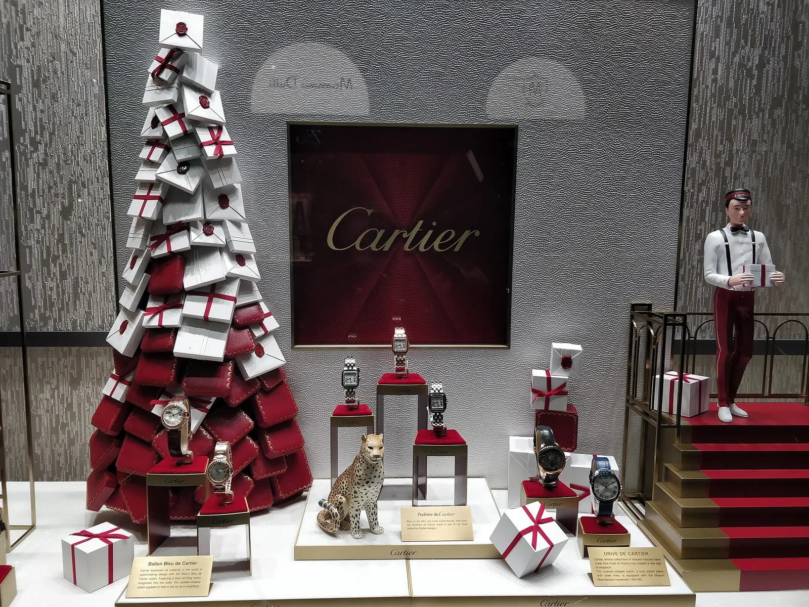 カルティエの店頭ウィンドウ。積み上げたギフト箱と豹の陶製の置物、台の上に数本の腕時計が英文の説明札とともに並ぶ