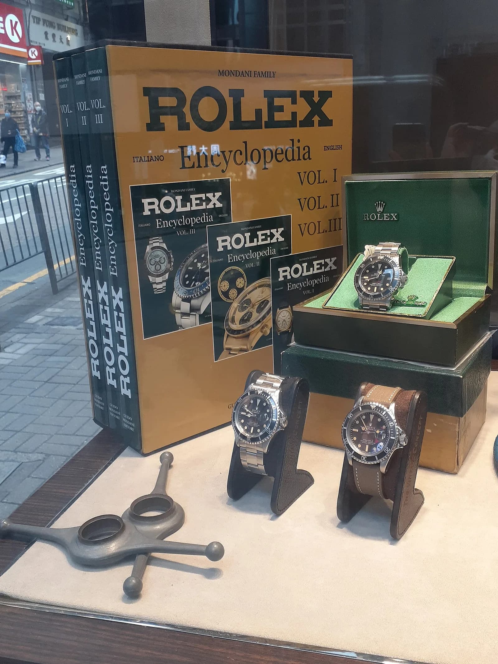 香港の時計店のウィンドウ。緑色の箱と数冊の書籍、スタンドに載った二本のヴィンテージの潜水用モデルが並び、ガラスに街が映り込んでいる