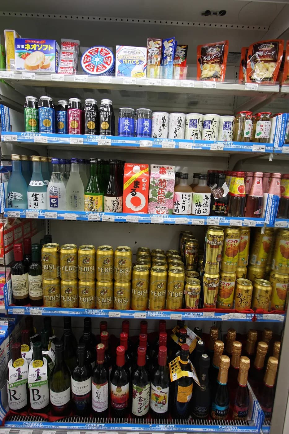 コンビニの酒類冷蔵ケース。ヱビスの金色の缶が並び、上段に日本酒、下段にワインが見える