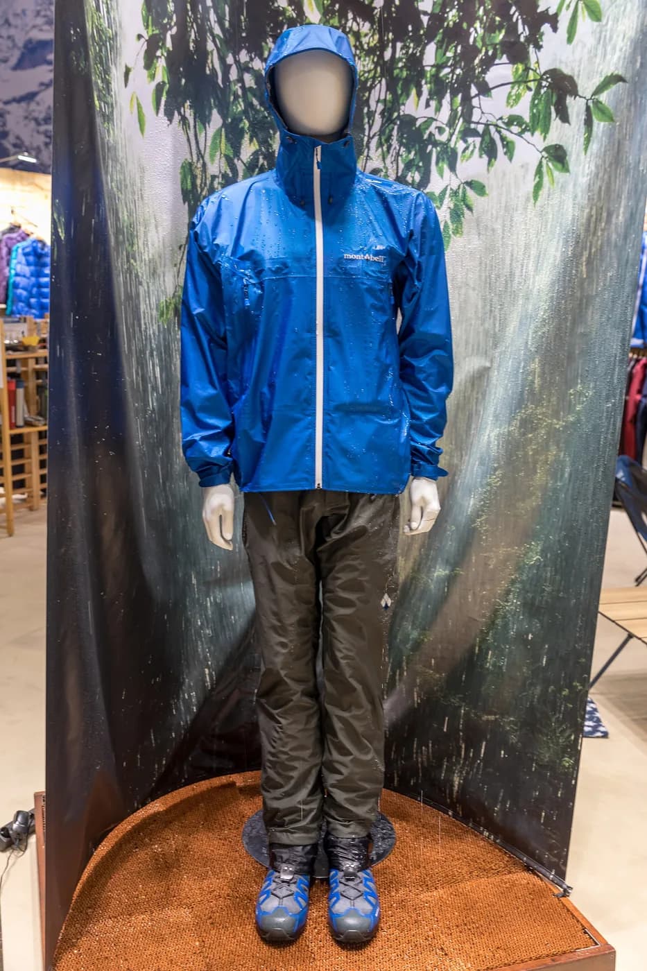 展示ブースのマネキンが着た青いmont-bellのレインジャケット。胸に白いロゴ、表面に水滴