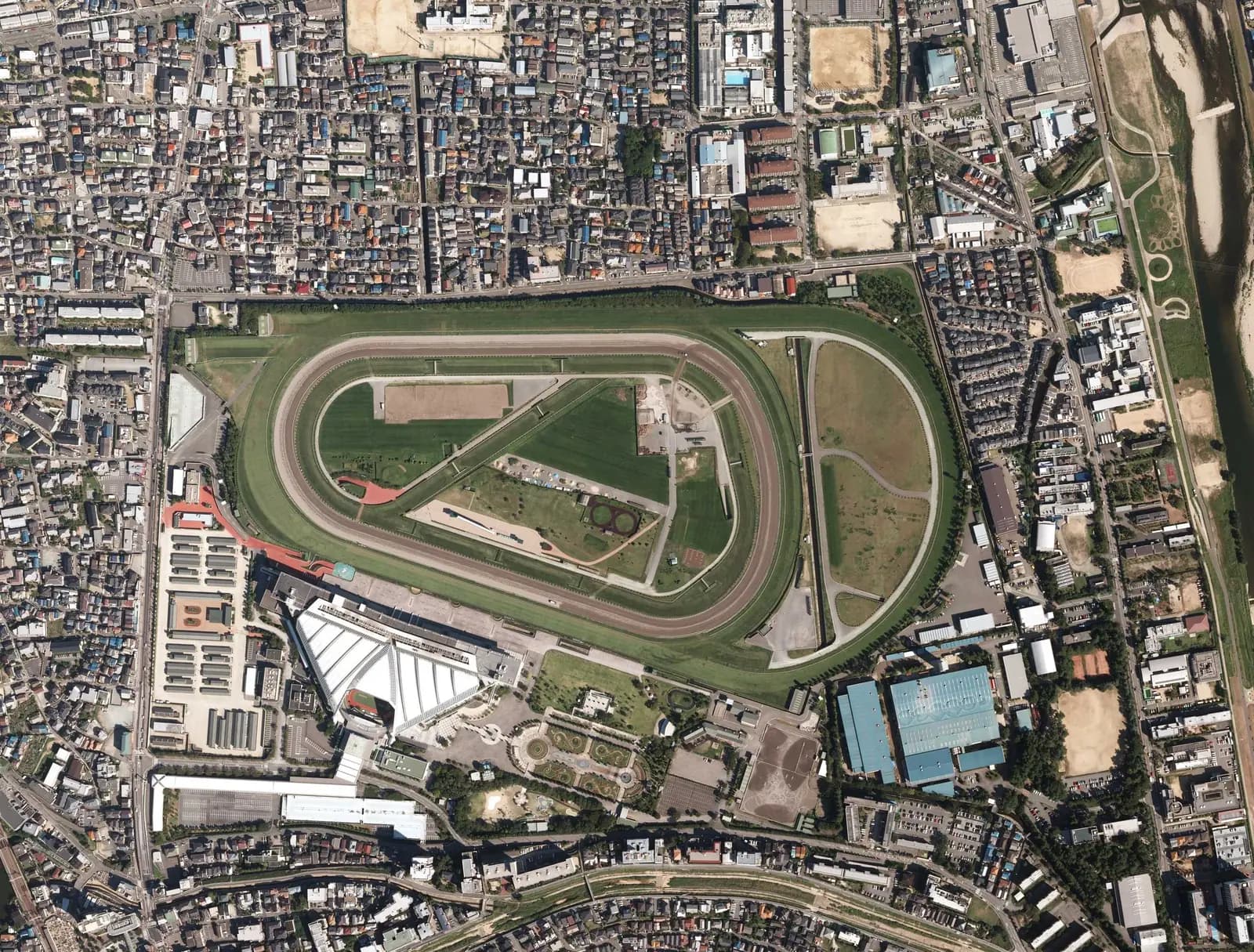上空から見た阪神競馬場。外側に大きくふくらむ芝コースと、その内側をまわる芝コース、さらに内側のダートコースが見え、左下にスタンドがある