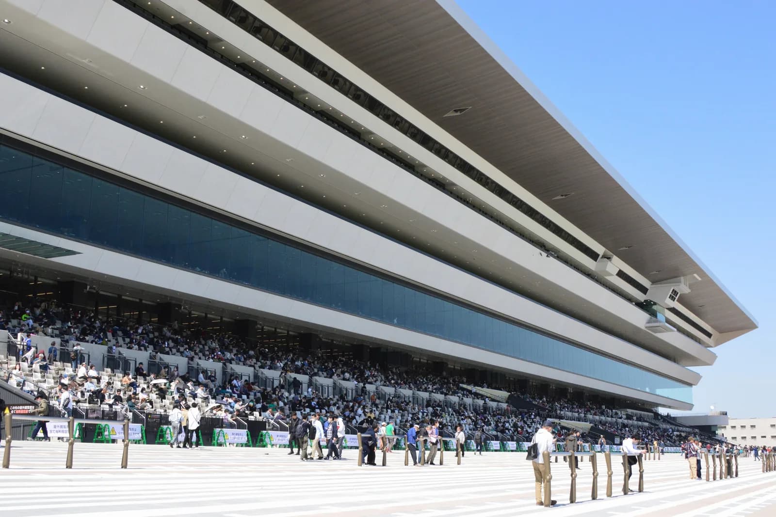 2023年に建て替えられた京都競馬場のスタンド。大きく張り出した庇の下に段状の観覧席があり、多くの人が座っている