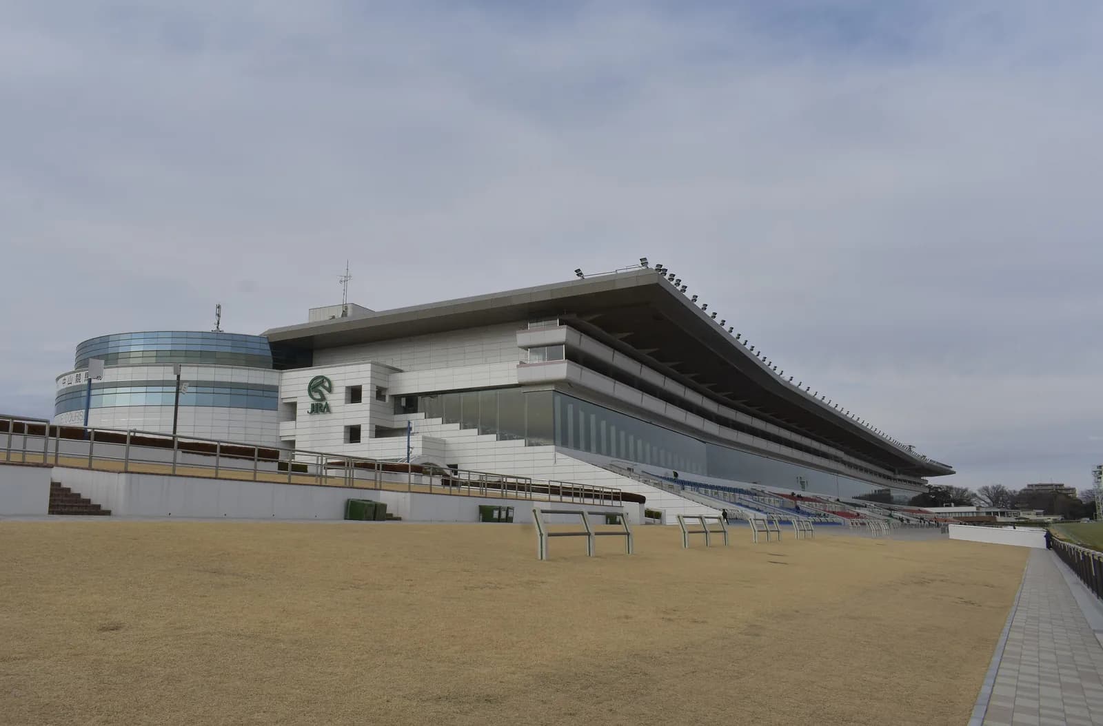 中山競馬場のスタンドを馬場の側から見た写真。冬で草は枯れ色、観客はいない