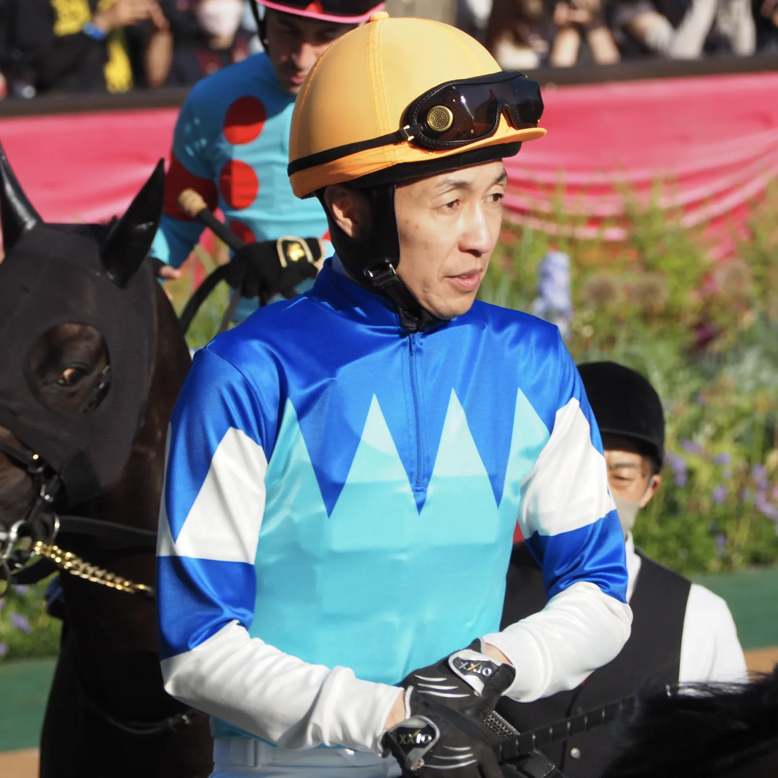 騎手の服とヘルメット姿の武豊が、馬に乗って発走前の下見所を周回している。ゴーグルはヘルメットに上げている