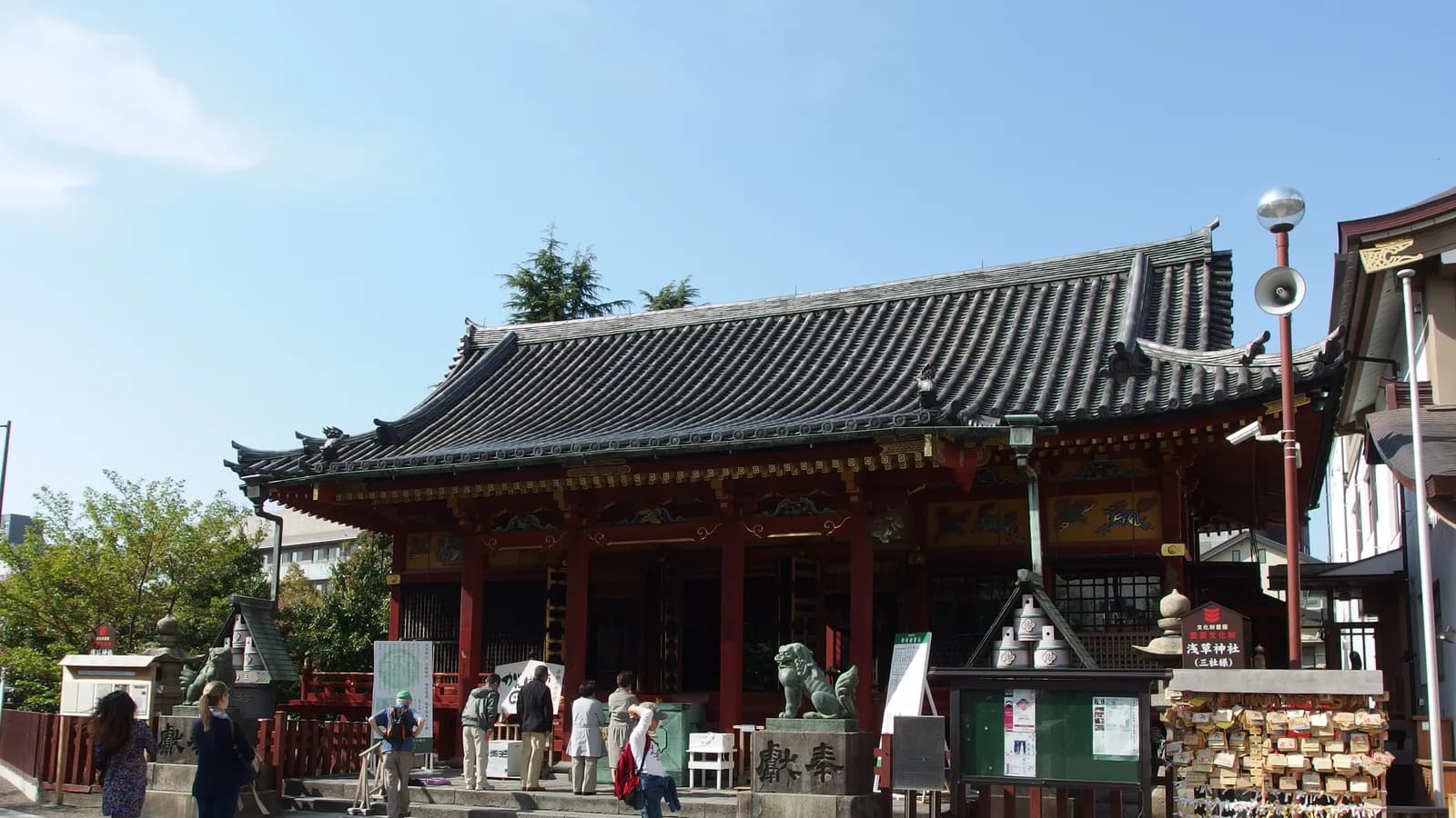 浅草神社の社殿。黒い瓦屋根が段になって連なり、朱塗りの柱の上、軒の下に金と緑で彩色された板がはまっている