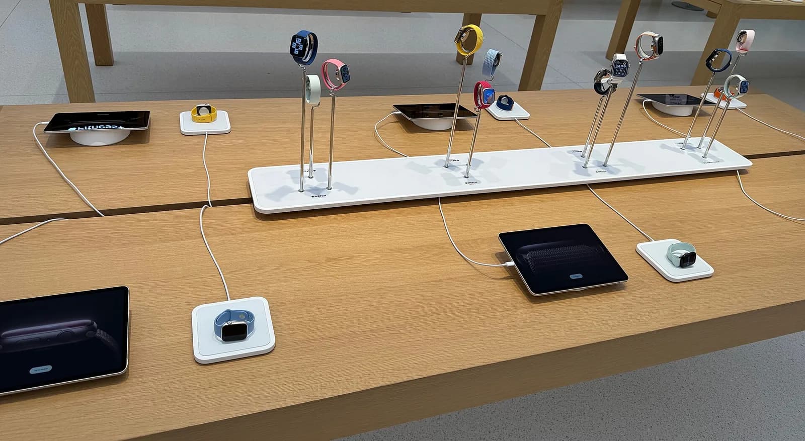店舗の木製テーブルに、スタンドと充電パッドで並べられた十数本のApple Watch。それぞれ色の違うバンドが付いている。人物は写っていない