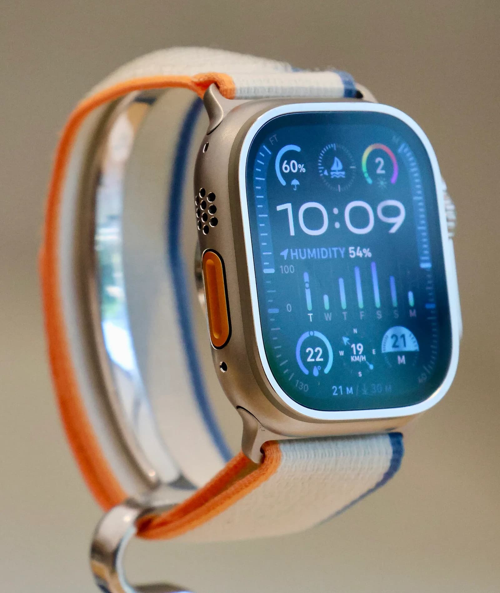 チタンのケースに橙色のボタンが付いた大型のApple Watch Ultra 2。白と青の布製バンドが付いている。斜めからの接写