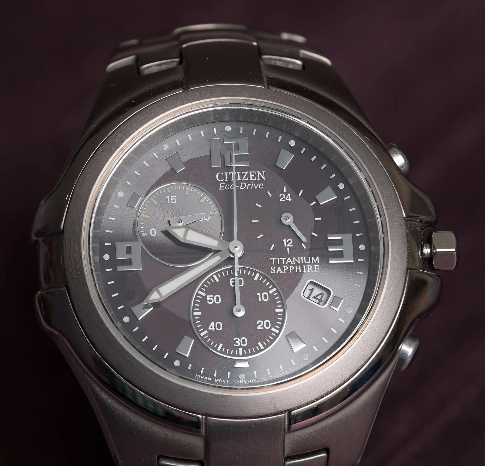 濃い灰色の文字盤に三つの小さな円と日付窓を持つチタン製のクロノグラフ。文字盤に TITANIUM SAPPHIRE の表示がある