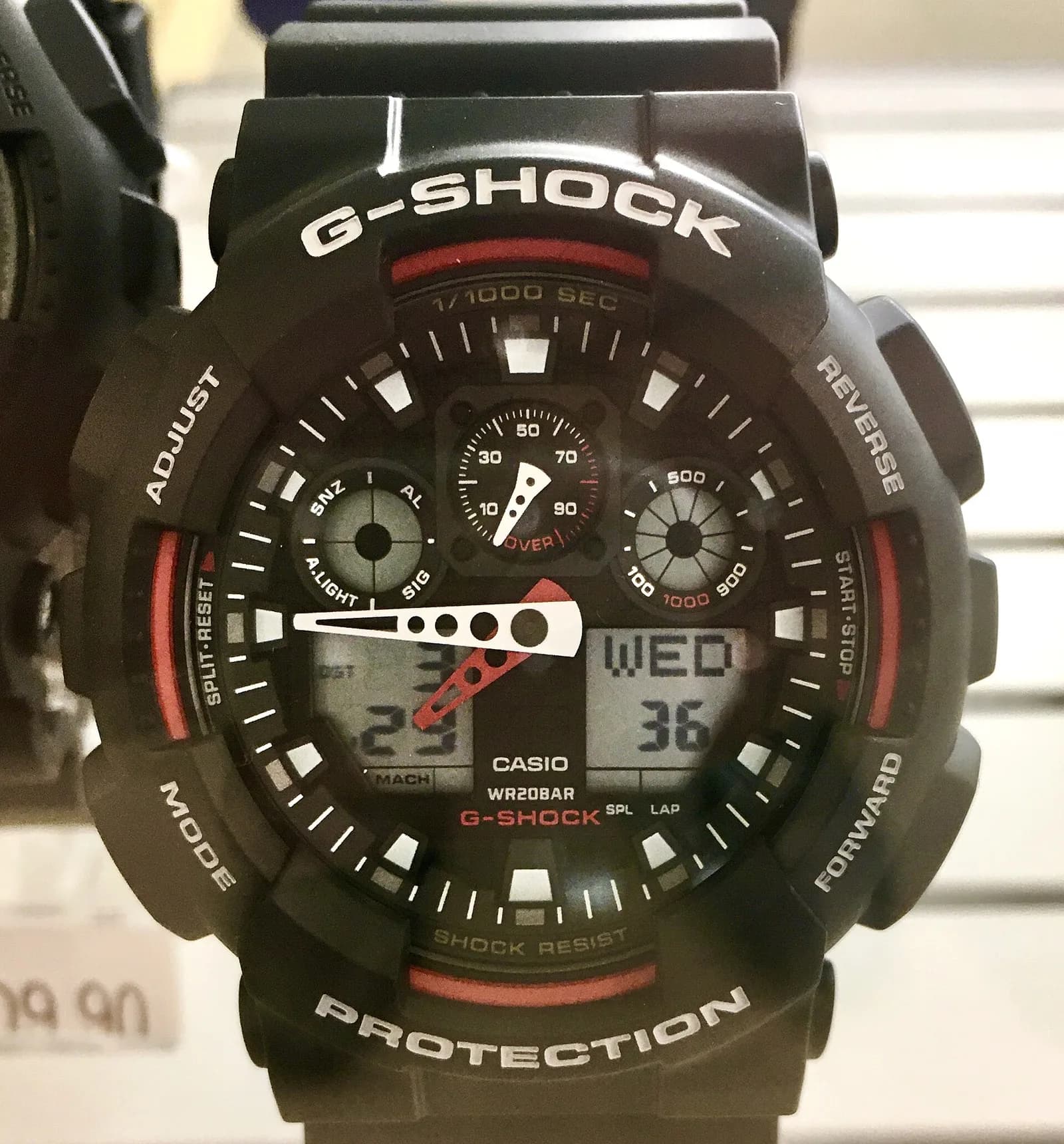 店頭の陳列棚に置かれた大型のアナログとデジタルを併せ持つG-SHOCK。針と二つの液晶窓、赤い差し色、ベゼルに刻まれた文字が見える