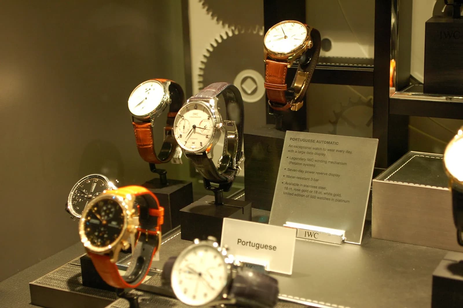 店舗のショーケースに並んだ複数のIWCポルトギーゼと、それぞれに添えられた説明カード。暖色の照明が当たっている