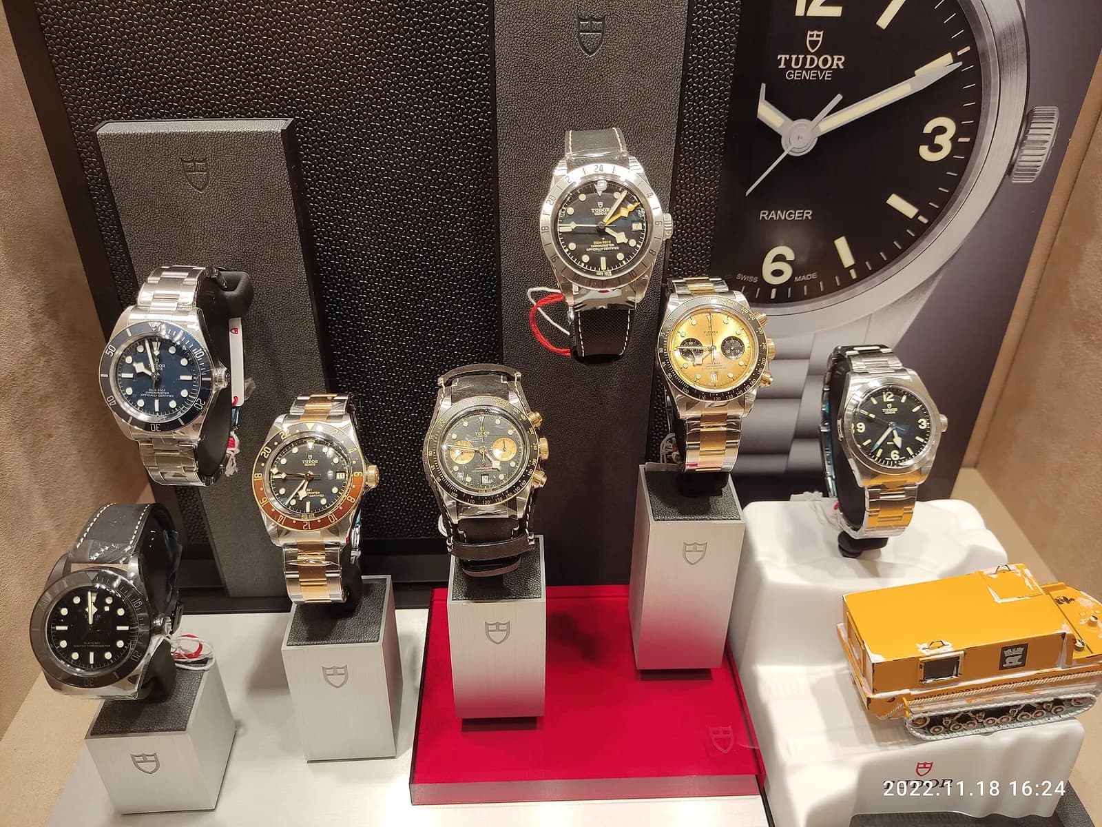 時計店のウィンドウ。スタンドに並んだ7本のチューダーと、右上に大きな壁掛け時計。ケースには盾のロゴが並ぶ